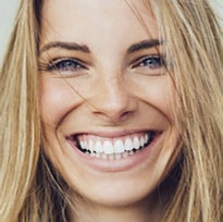 Close up of woman with blonde hair smiling with great looking teeth and healthy gums.